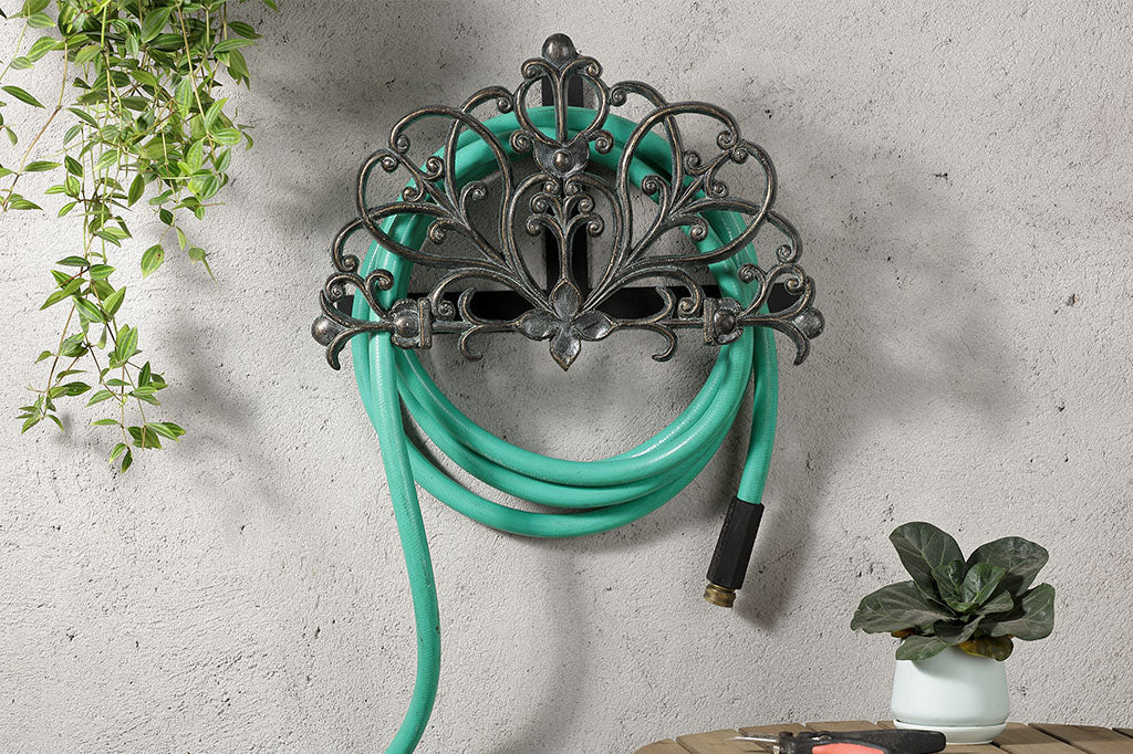 Rouleau Hose Holder mounted to a wall in a garden near a table. It holds a green hose
