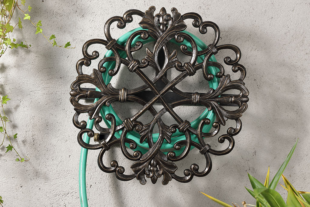 Fontaine hoseholder with scrollwork accents has a hose coiled around it and mounted to a wall