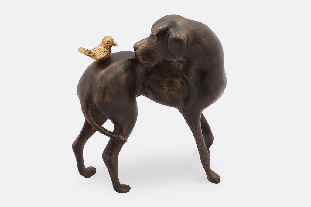 cast metal garden sculpture of dog looking at a bird on its back