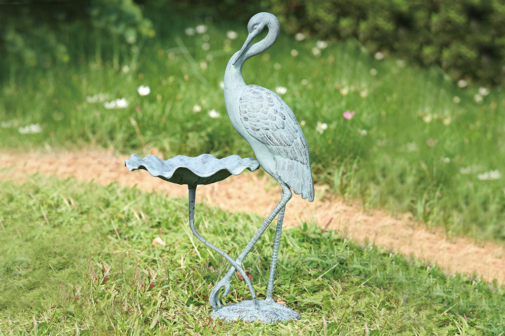 birdfeeder in garden in shape of flower blossom with standing crane sculpture