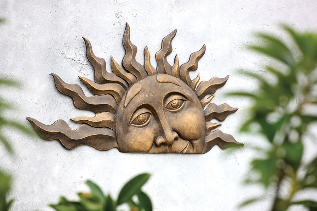 half sun, as if it is setting, sculptural wall plaque on a cement wall in yard