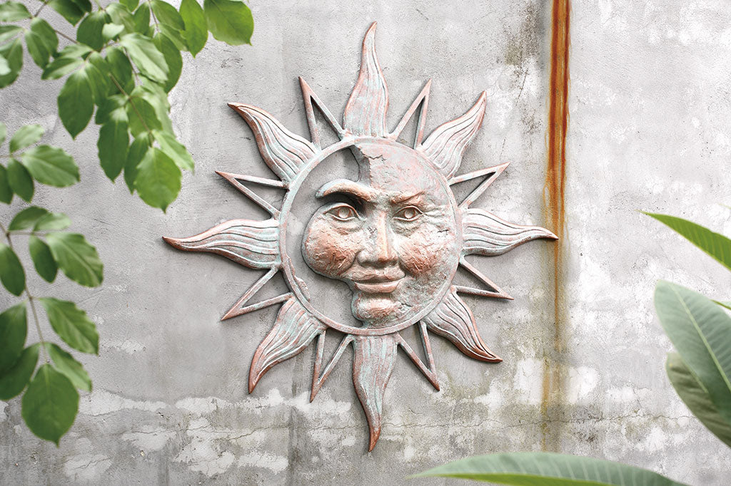 cast metal sun wall plaque on rusty concrete wall by tree