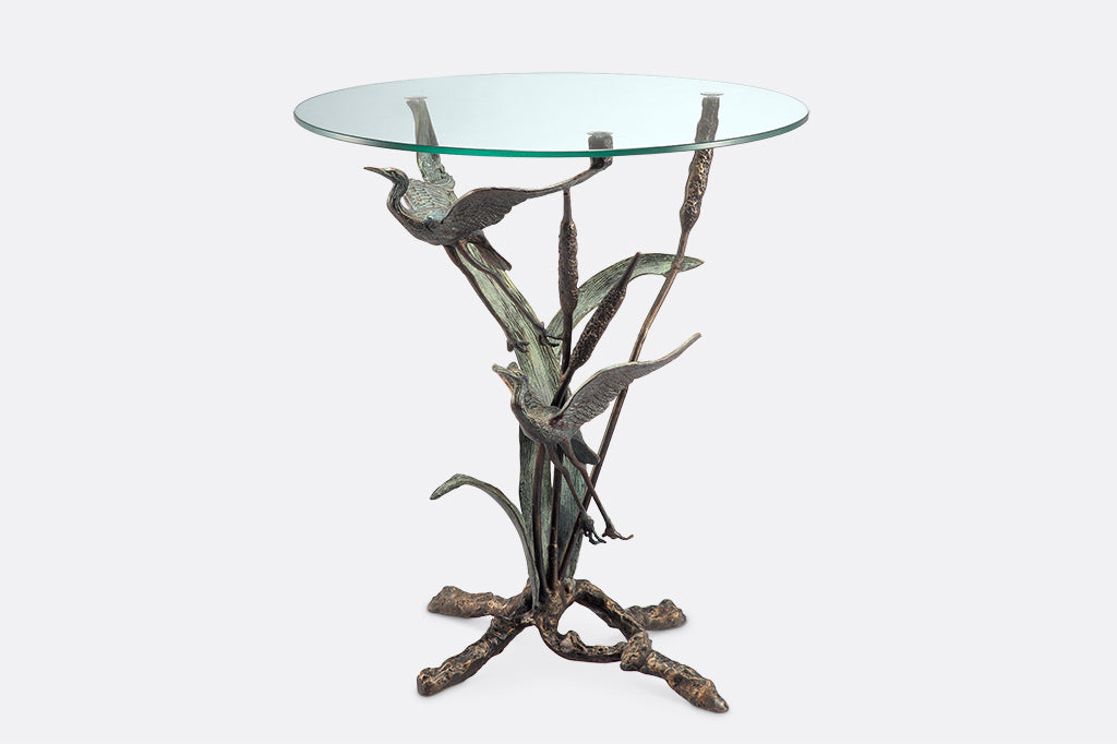 drink table with glass top supported by sculpture of flying cranes and cattails