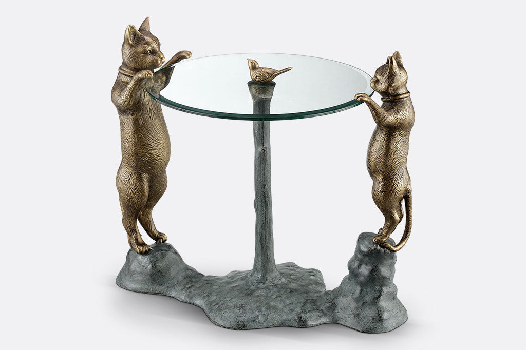 cats peek at a bird finial in a decorative glass topped table