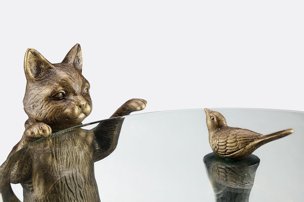 cat peeks at a bird finial in a decorative glass topped table