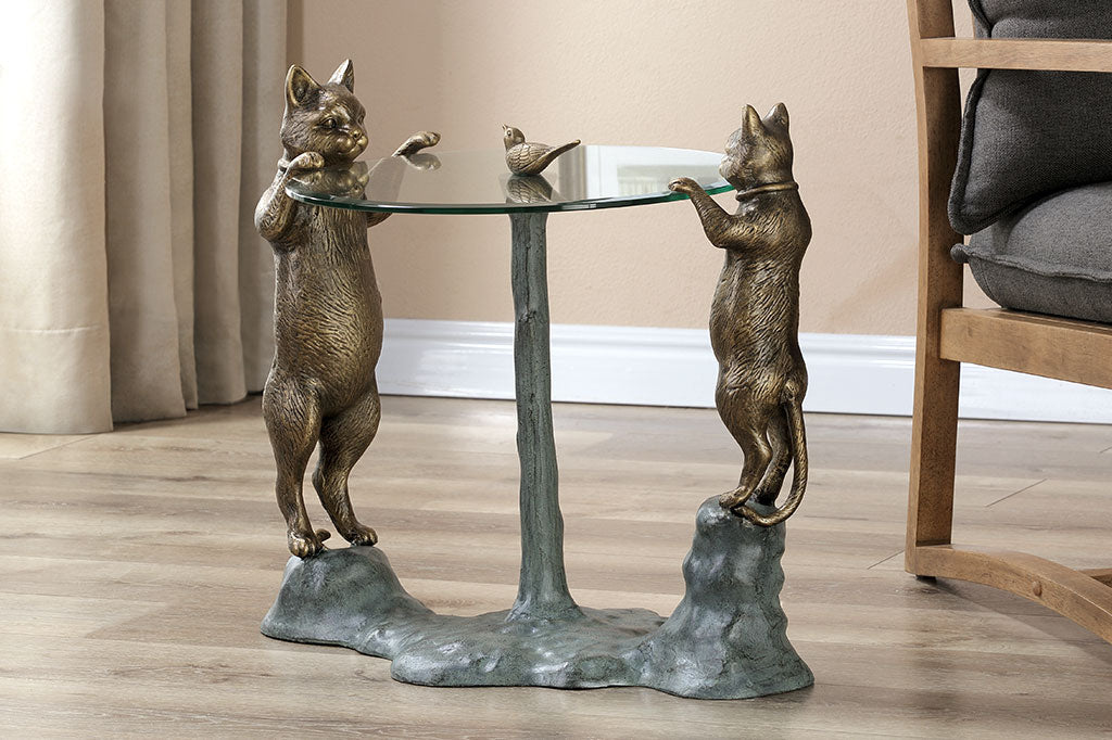 cats peek at a bird finial in a decorative glass topped table