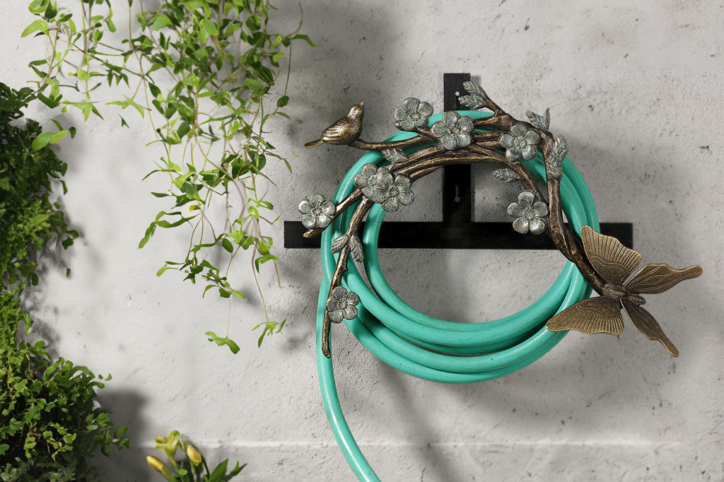 Papillion Hose Holder holding a green hose on a wall in the garden