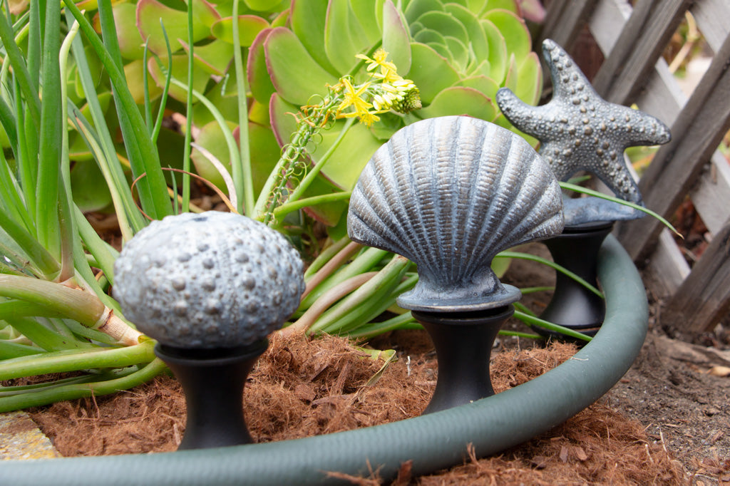 Three coastal themed hose guards in the soil by a hose