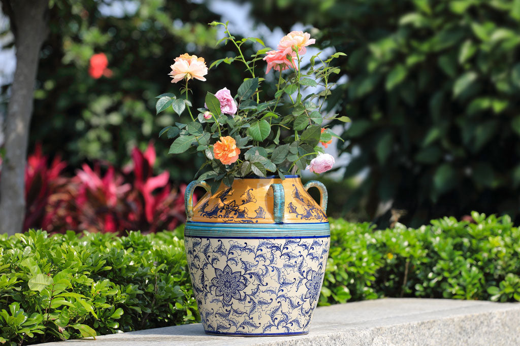 hand painted and thrown ceramic pot with mediterranean prints done in vivid yellow-orange, light and dark blue with floral print on white - shown in rose garden