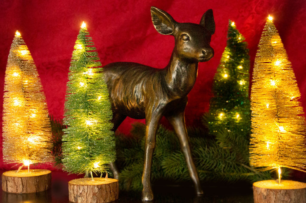 cast metal fawn sculpture set in Christmas scene, bottle bristle green and gold trees with winter juniper branches