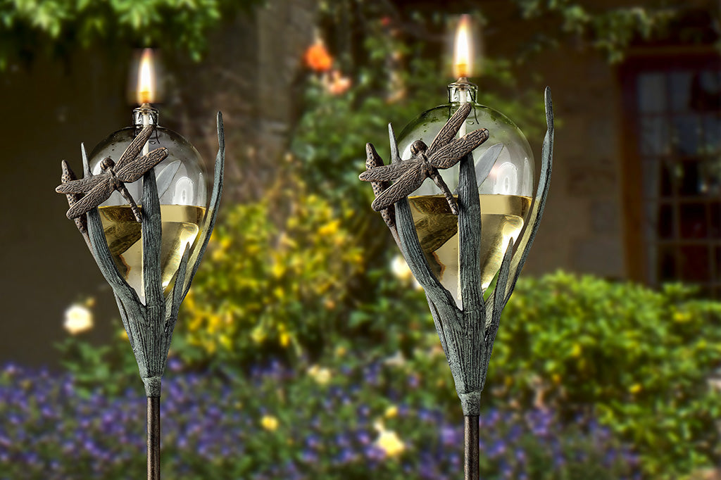dragonfly and frond sculpted motif on glass oil torch - two shown in dusky garden scene