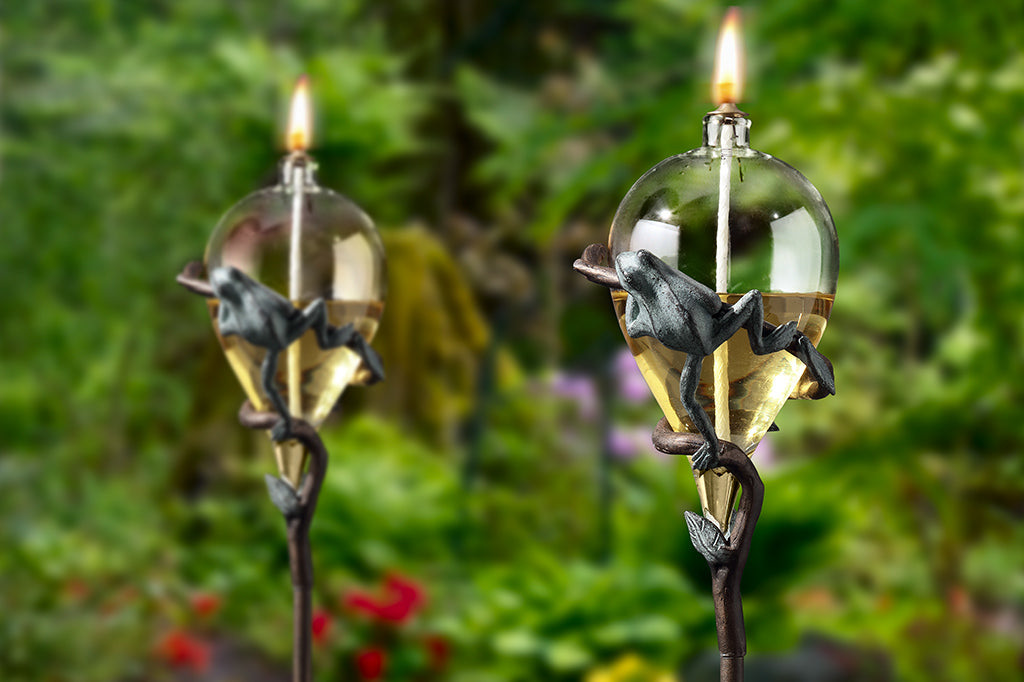 staked glass oil torch with frog on vine motif - shown in garden as a pair of 2 with frog's back facing viewer