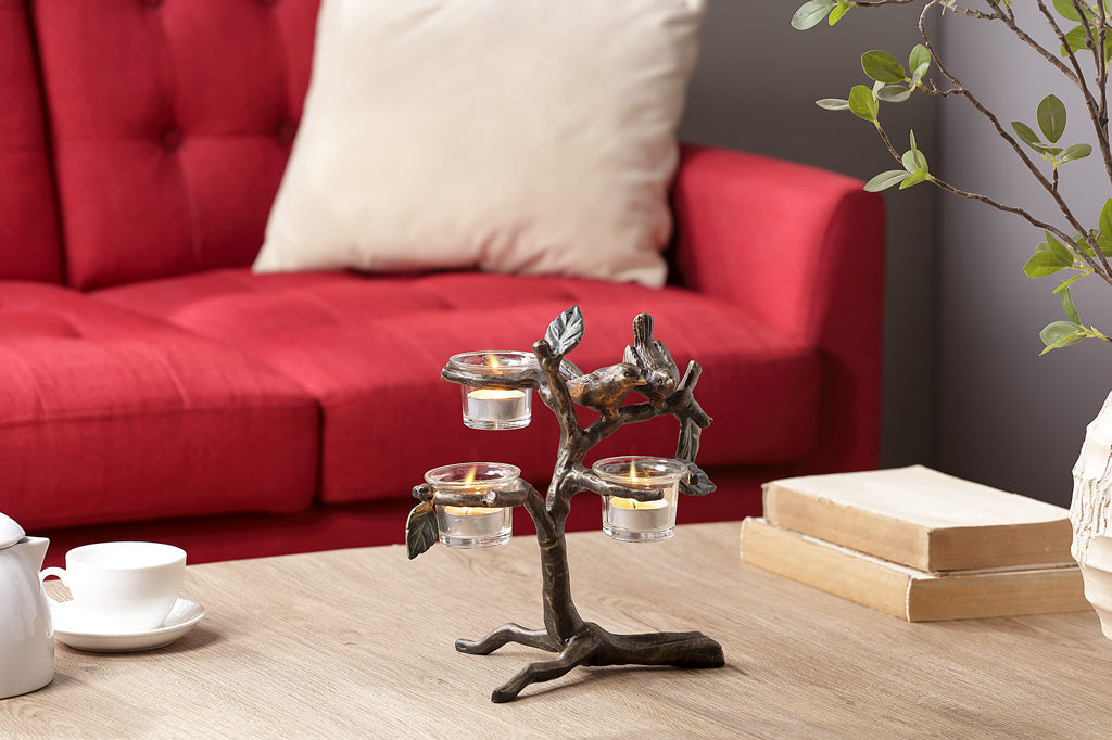 small bird and branch table candelabra with 2 birds, holds 3 tealights in glass cups shown on coffee table near red couch