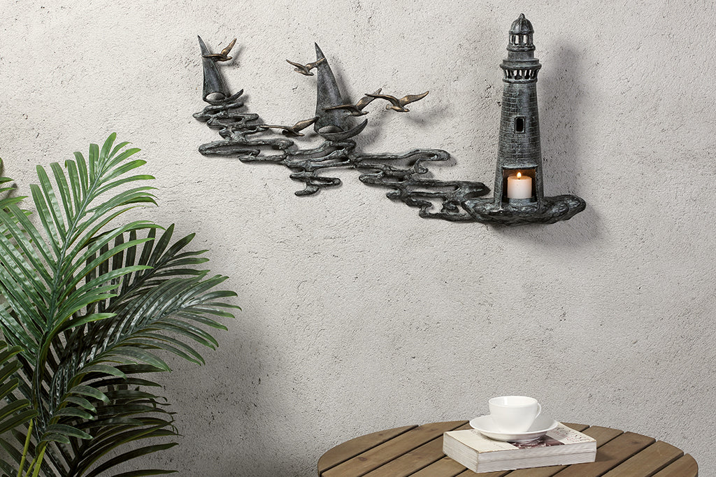 Wall art Votive holder cast metal sculpture of Lighthouse by the sea with 2 sail boats on an outdoor wall by a café table and potted plant