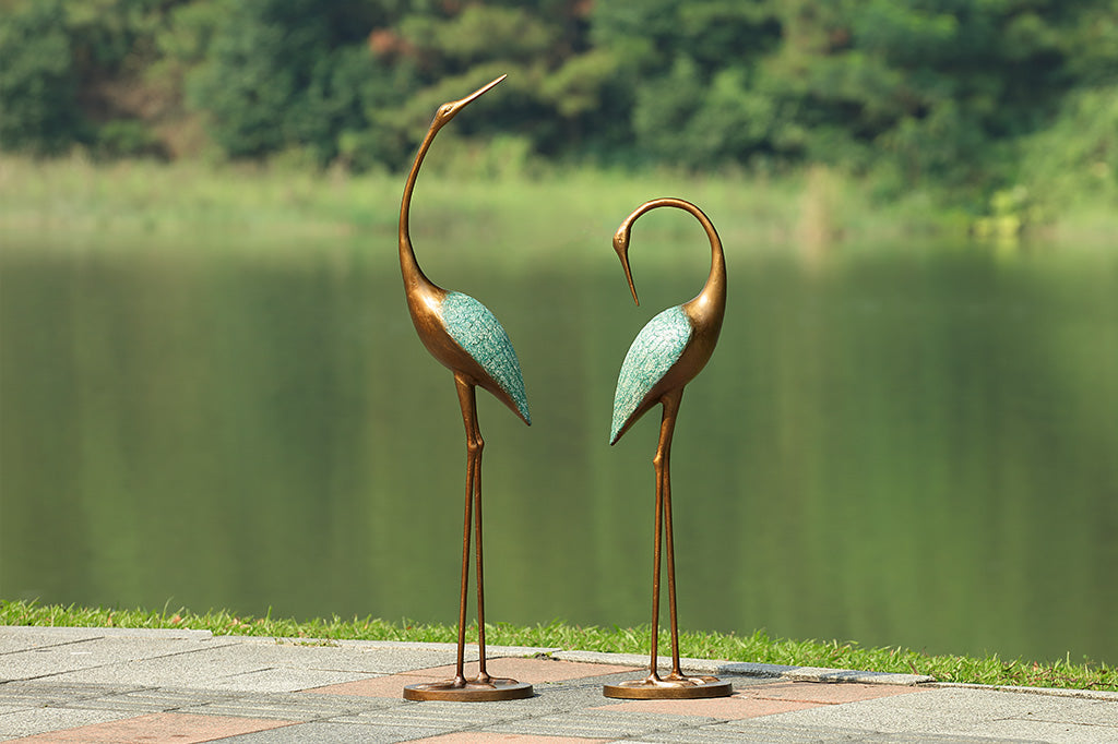 cast metal pair of cranes with blue detailing on feathers set in front of lake