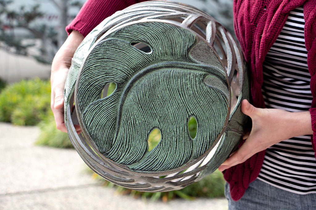 woman holds palm leaf theme garden stool to show the top motif of verdi color leaf