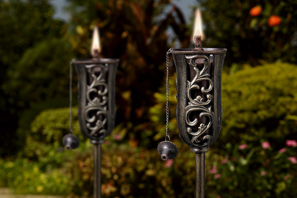cast metal oil torch with swirling details and cap for oil torch wick set in garden scene