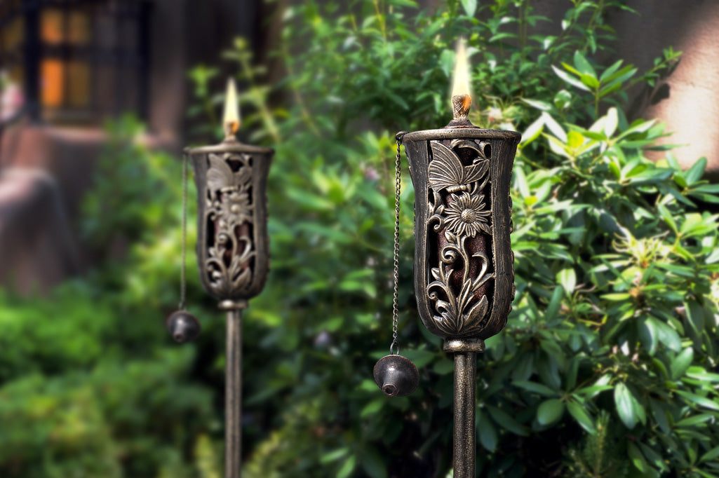 cast metal oil torch with butterfly and flower detailing set in garden