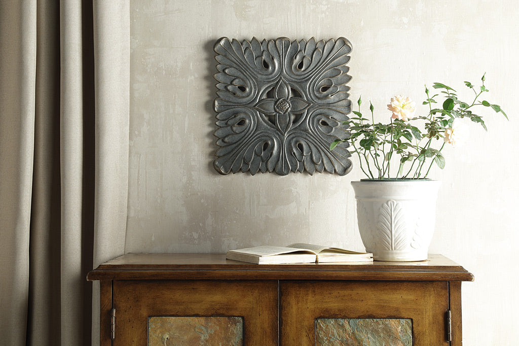 cast metal wall plaque staged on wall above cabinet with potted plant