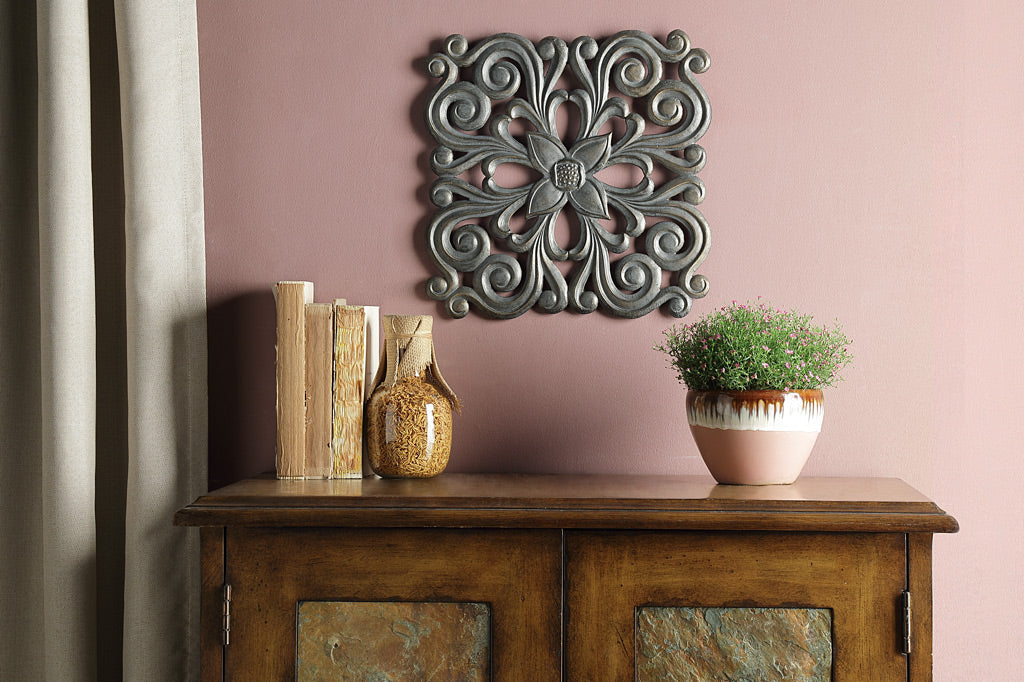 cast metal square wall plaque on maroon wall above cabinets next to window