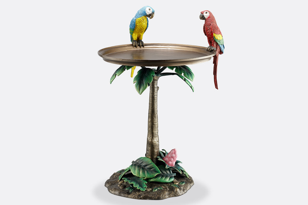 cast metal table with two colorful parrots perched on table edge, the base of the table is a palm tree with green foliage