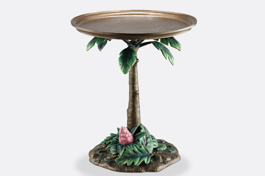 cast metal table the base of the table is a palm tree with green foliage