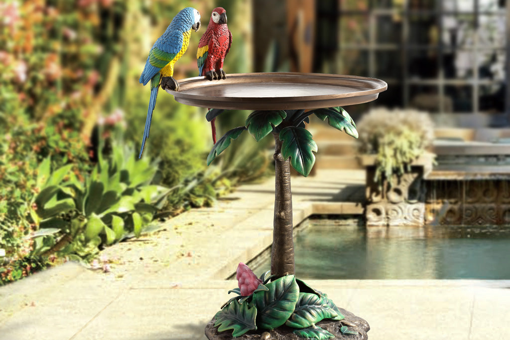 cast metal table with two colorful parrots perched on table edge, the base of the table is a palm tree with green foliage