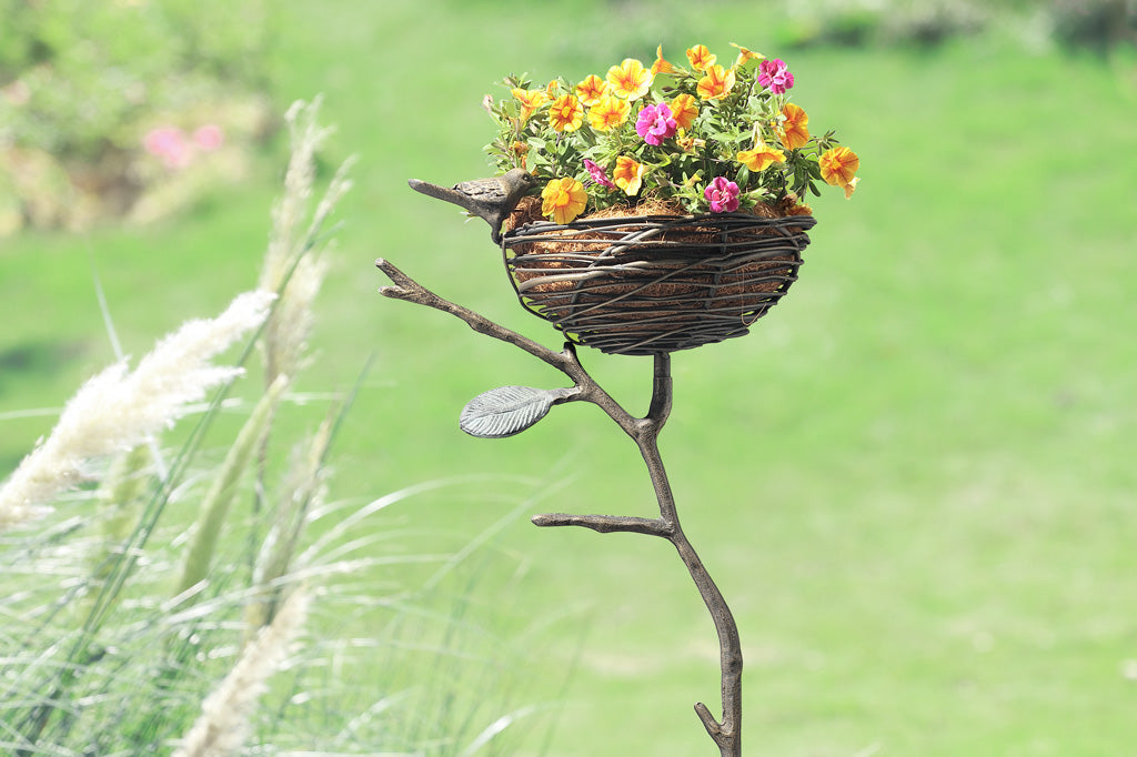 staked garden art that can hold items; shaped like a nest on a branch with decorative bird on rim placed in garden with pampas grass