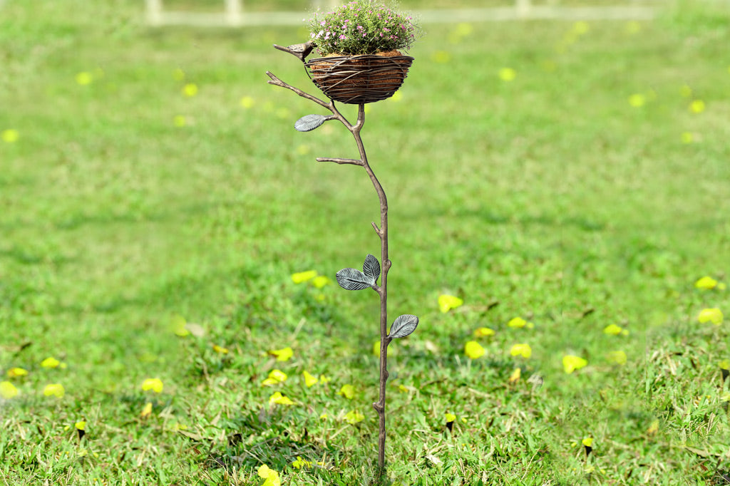 staked garden art that can hold items; shaped like a nest on a branch with decorative bird on rim placed in garden with grass
