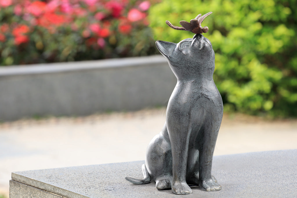 cast metal cat sculpture with dragonfly on tip of nose placed in garden setting