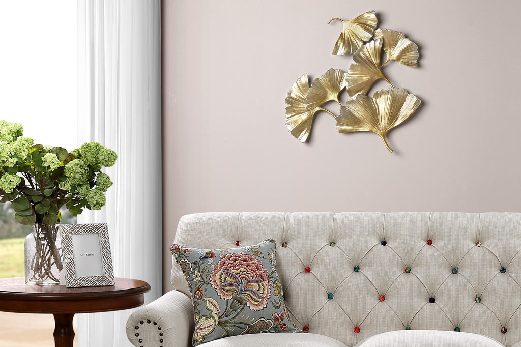 wall art featuring 6 golden scattered ginkgo leaves shown above tufted couch in living room