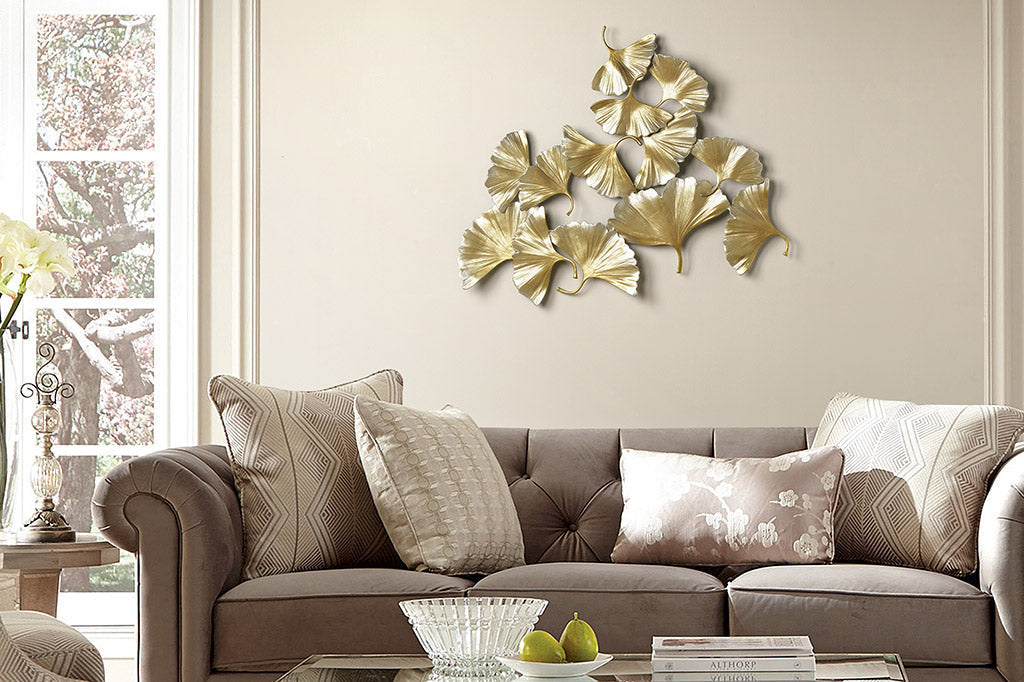 Golden wall art sculpture of 13 topsy turvy ginkgo leaves shown in living room above a couch