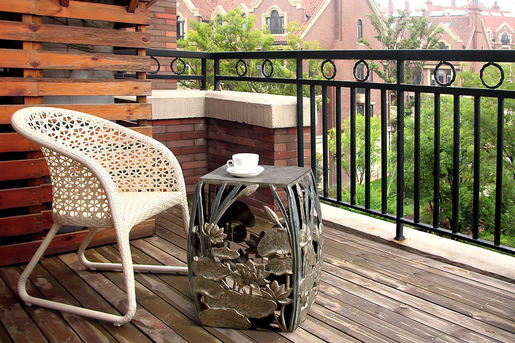 cast metal lotus flowers and cattails squared garden stool, floral design on all four panels of stool. Shown on porch next to outdoor chair with teacup resting on stool surface