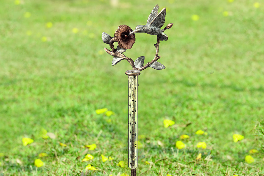 cast metal hummingbird and flower rain catcher set in grassy field