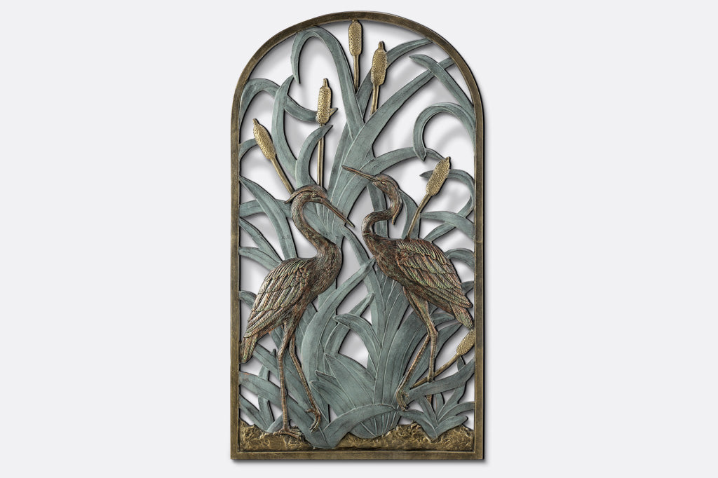 arched wall plaque features two herons standing amongst cattails