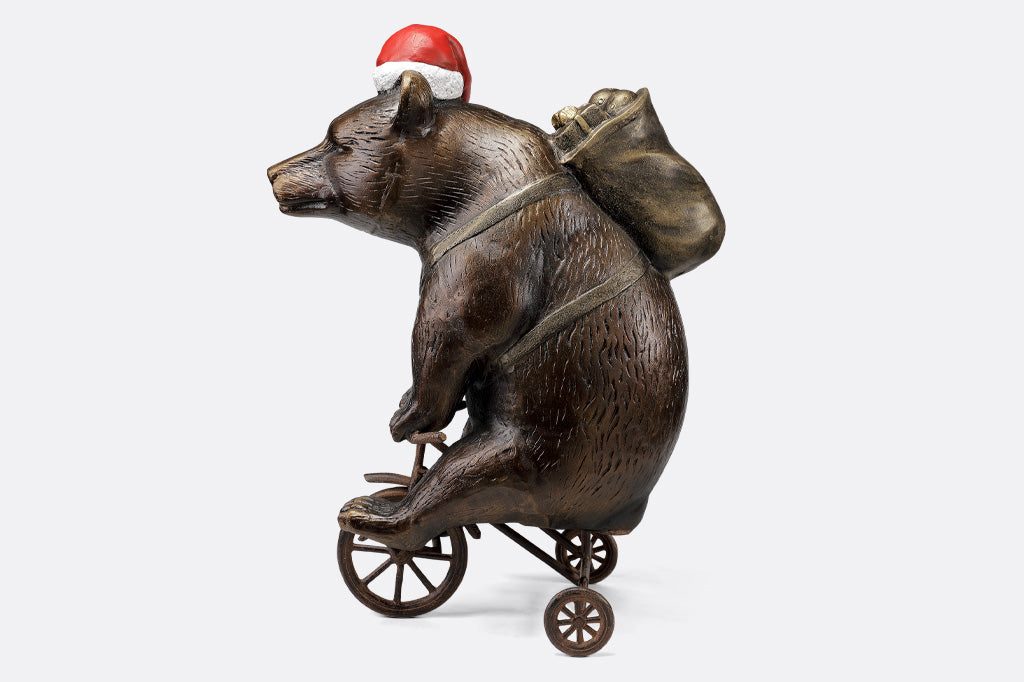 cast aluminum bear riding a tricycle with present on their back and wearing a santa hat