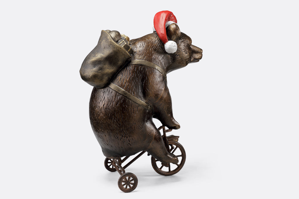 cast aluminum bear riding a tricycle with present on their back and wearing a santa hat