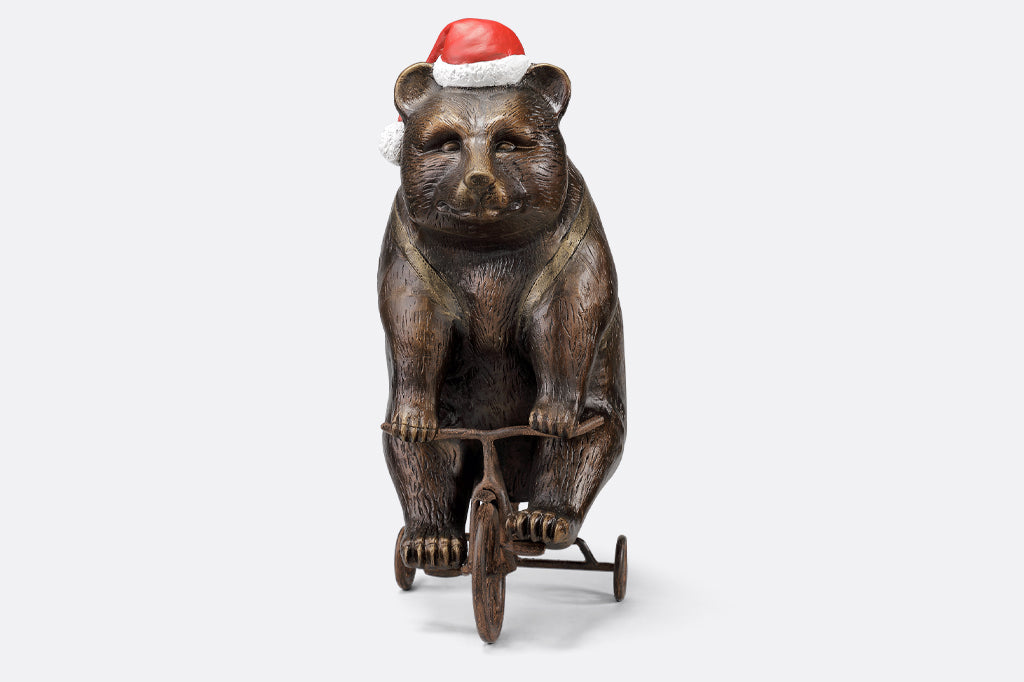 cast aluminum bear riding a tricycle with present on their back and wearing a santa hat