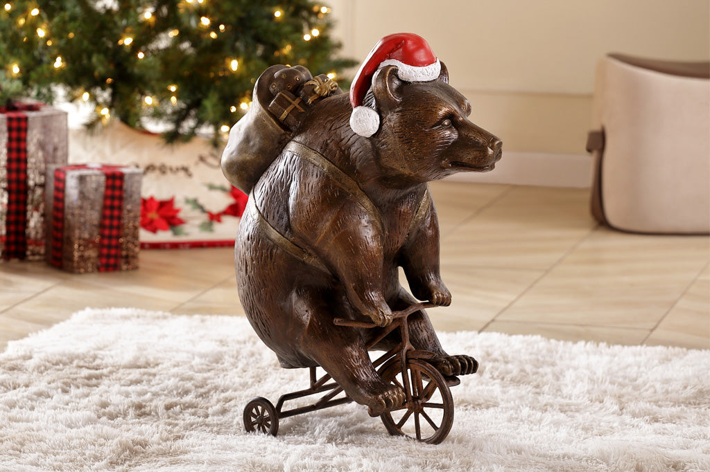 cast aluminum bear riding a tricycle with present on their back and wearing a santa hat. Set in holiday living room next to Christmas tree