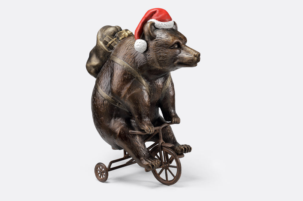 cast aluminum bear riding a tricycle with present on their back and wearing a santa hat
