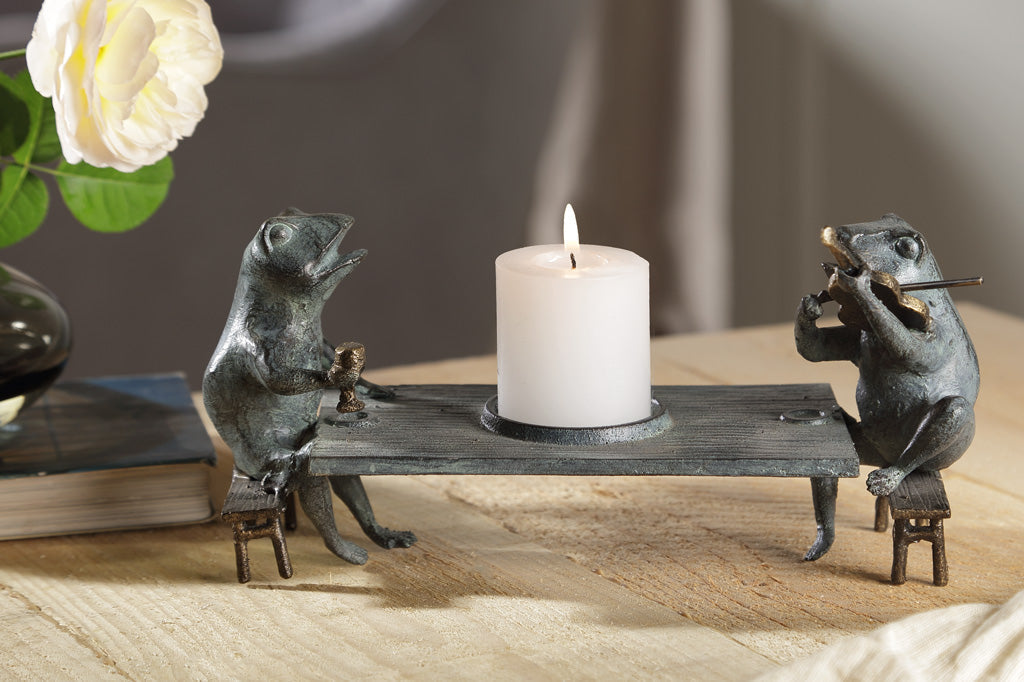 Candleholder sculpture of two frogs at a dining table; one plays violin while the other frog holds goblet.