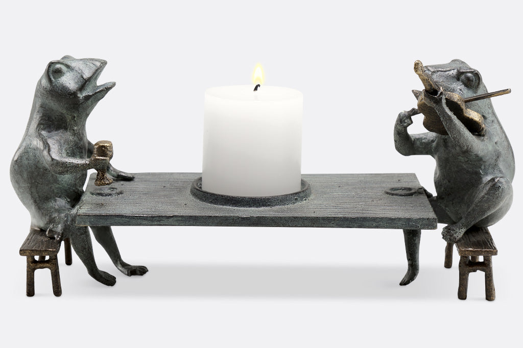 Candleholder sculpture of two frogs at a dining table; one plays violin while the other frog holds goblet.