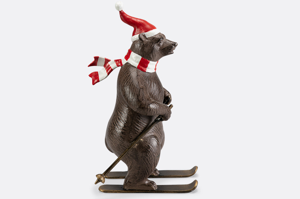A bear wearing a santa hat and striped scarf is skiing as part of a holiday table display