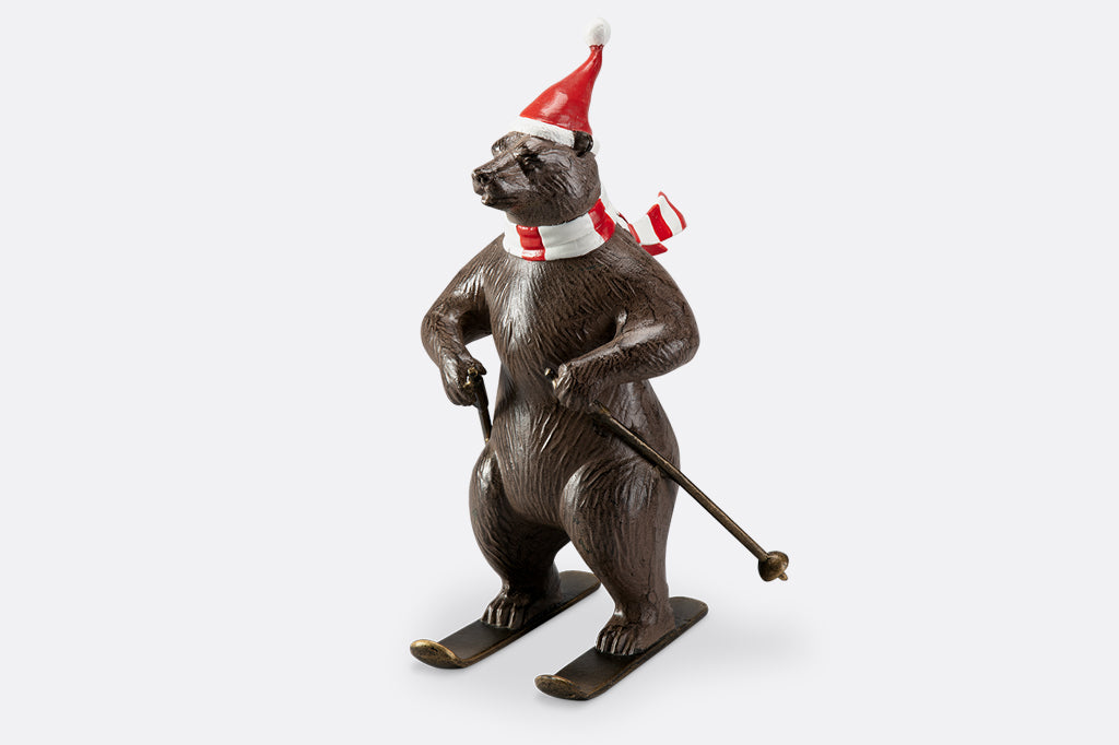 A bear wearing a santa hat and striped scarf is skiing as part of a holiday table display