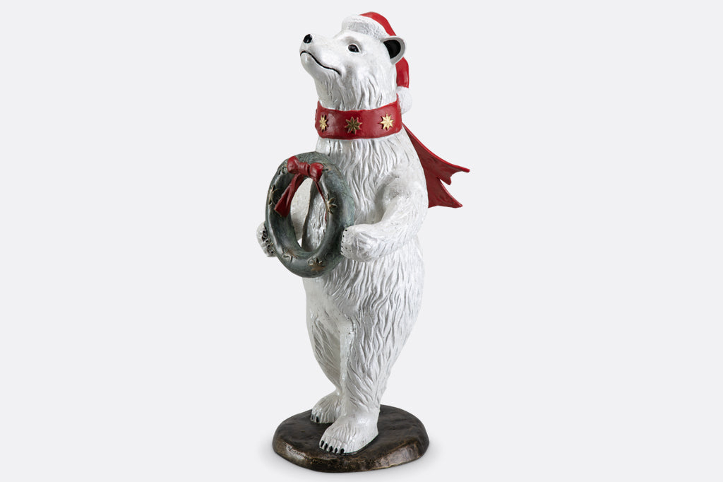 Polar bear wearing had and scarf holding wreath sculpture