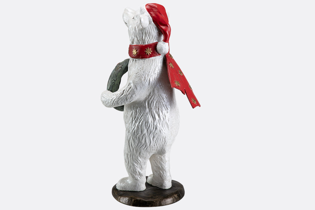 Polar bear wearing had and scarf holding wreath sculpture