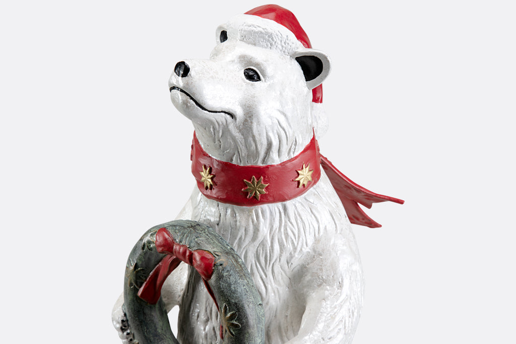 Polar bear wearing had and scarf holding wreath sculpture
