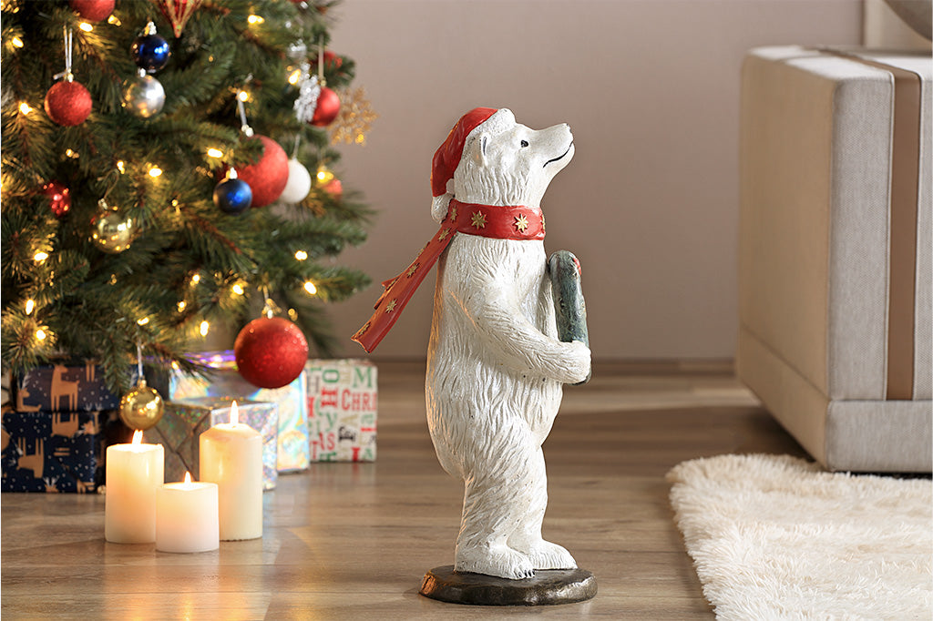 Polar bear wearing had and scarf holding wreath sculpture