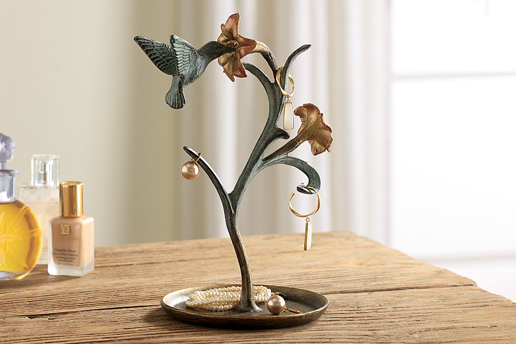 jewelry holder shaped like growing lily with humming bird visiting it. It holds rings and earrings on a vanity table with makeup and polish.