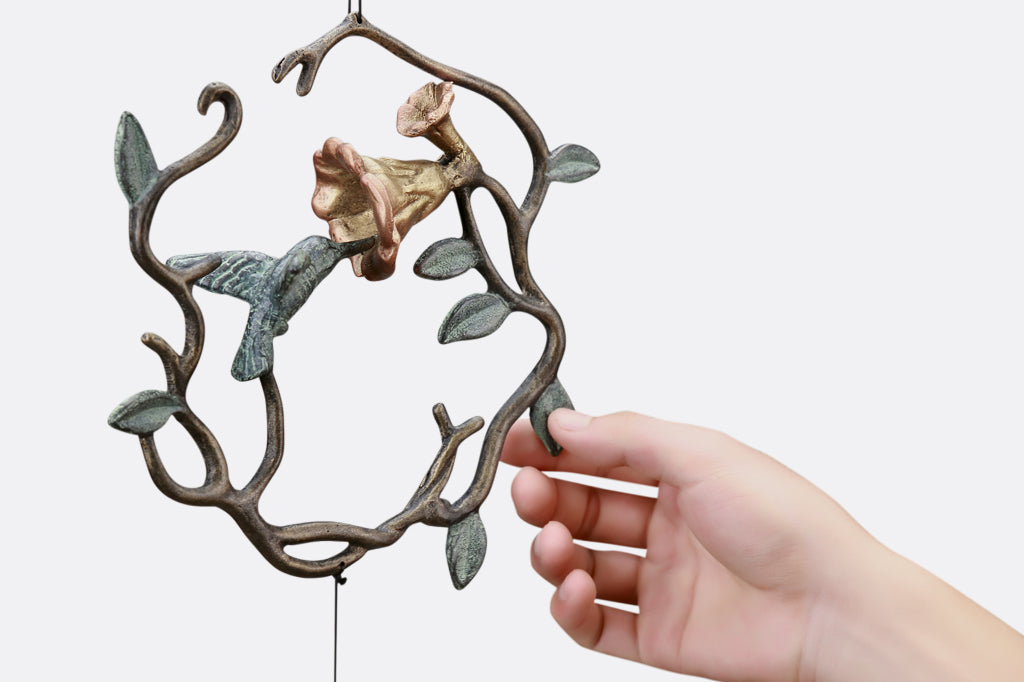 sculpted metal wind art with motif of encircled lily and hummingbird with 3 lily blossoms suspended below with a hummingbird pendant